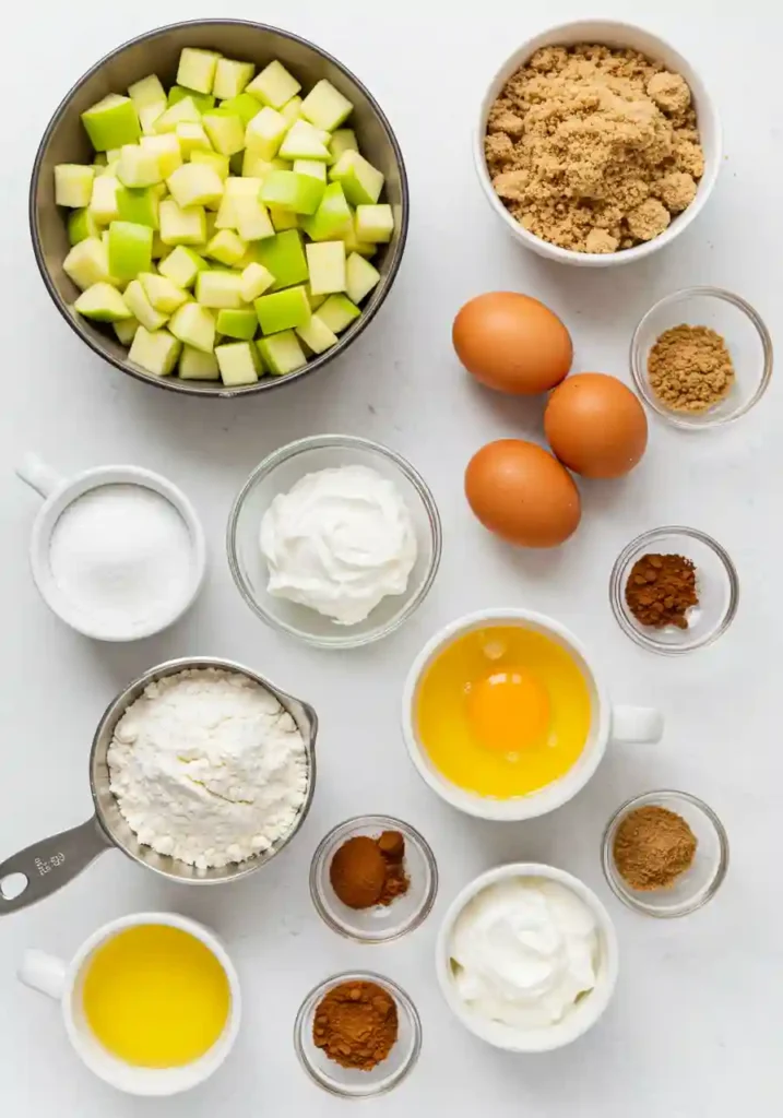All ingredients for apple pie cupcakes including flour, spices, fresh apples, butter, and eggs arranged on marble countertop