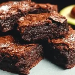 Stack of rich, fudgy avocado brownies cut into squares on a white plate with chocolate chips scattered around