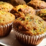 Golden brown banana zucchini muffins arranged on white plate with fresh zucchini and bananas in background