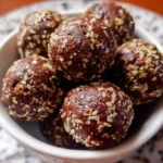 Homemade chocolate energy balls arranged on white plate with cocoa powder dusting and chia seeds scattered around