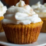 Golden pumpkin pie cupcakes with fluffy tops and creamy frosting arranged on a rustic wooden board