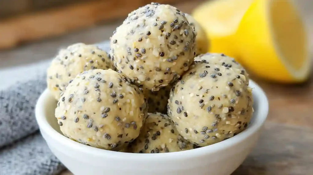 Golden no-bake lemon poppyseed protein balls arranged on a white plate with fresh lemon slices and poppy seeds scattered around