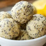 Golden no-bake lemon poppyseed protein balls arranged on a white plate with fresh lemon slices and poppy seeds scattered around