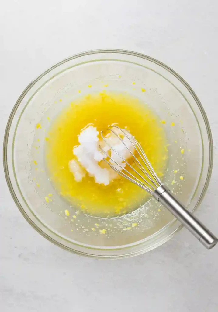 Hands pouring wet lemon mixture into bowl of dry ingredients for no-bake protein balls, showing the mixing process