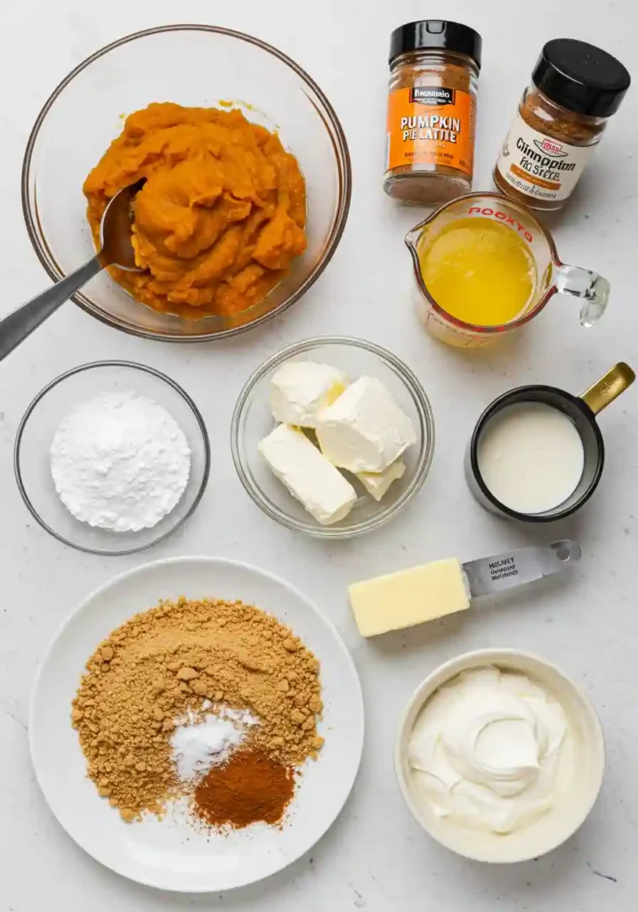 All ingredients for no bake pumpkin cheesecake laid out including cream cheese, pumpkin puree, graham crackers, spices, and heavy cream
