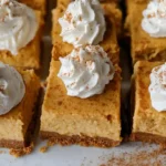 No bake pumpkin cheesecake bars with gingersnap crust cut into squares on a white plate with fall decorations