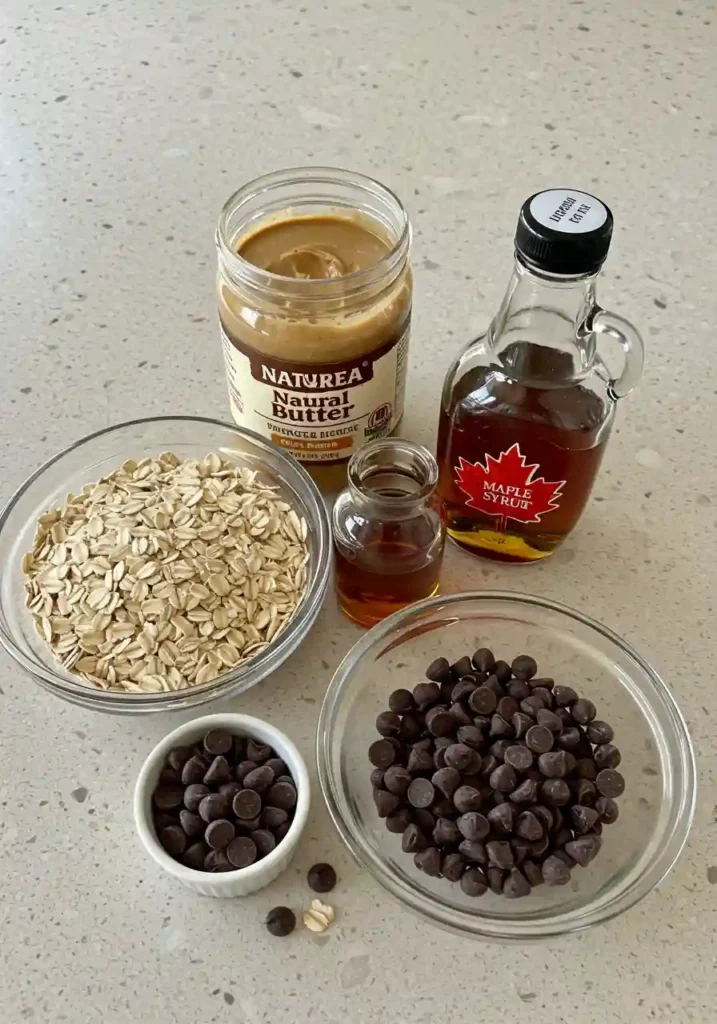 Measured ingredients in bowls – rolled oats, peanut butter, maple syrup, and chocolate chips