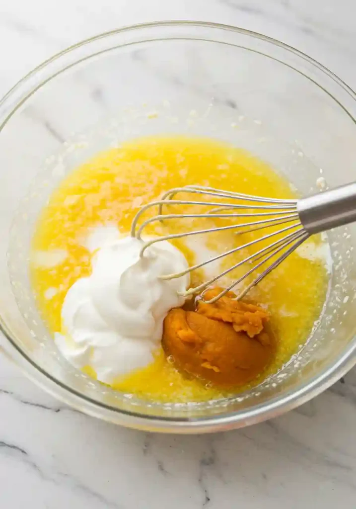 Combining pumpkin puree with wet ingredients in mixing bowl