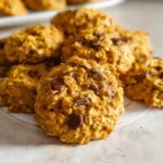 Stack of soft pumpkin oatmeal chocolate chip cookies on white plate with pumpkin and cinnamon sticks