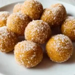 Stack of orange pumpkin protein balls on white plate with pumpkin spice scattered around and fall leaves in background