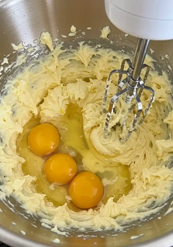 Electric mixer beating eggs into creamy butter and sugar mixture for cake batter