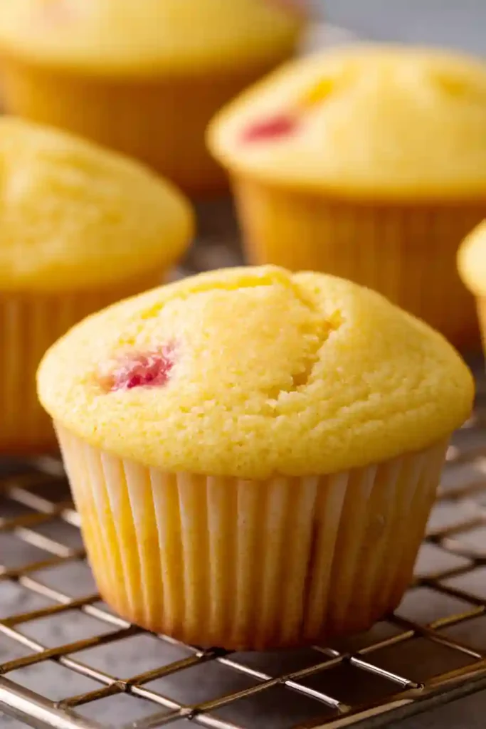 Golden strawberry lemonade cupcakes cooling on wire rack after baking, showing perfect dome tops and visible strawberry pieces