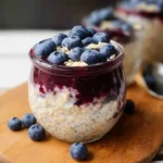 Creamy blueberry overnight oats in mason jar topped with fresh berries and almonds on marble surface