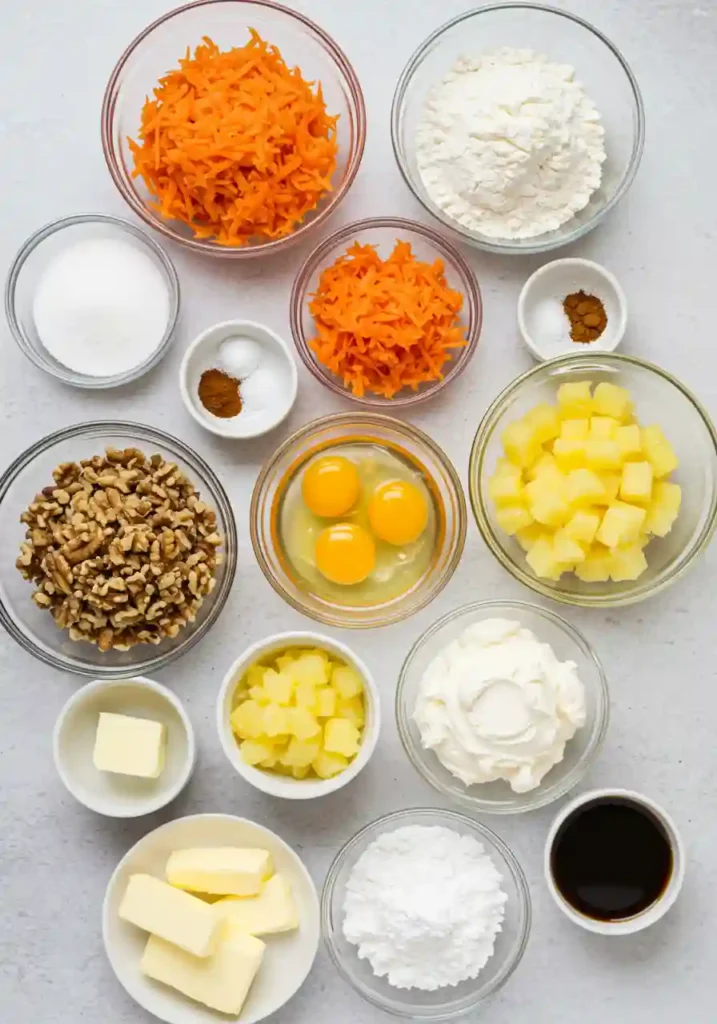 Carrot cake roll ingredients including fresh carrots, eggs, flour, cream cheese, and spices arranged on counter