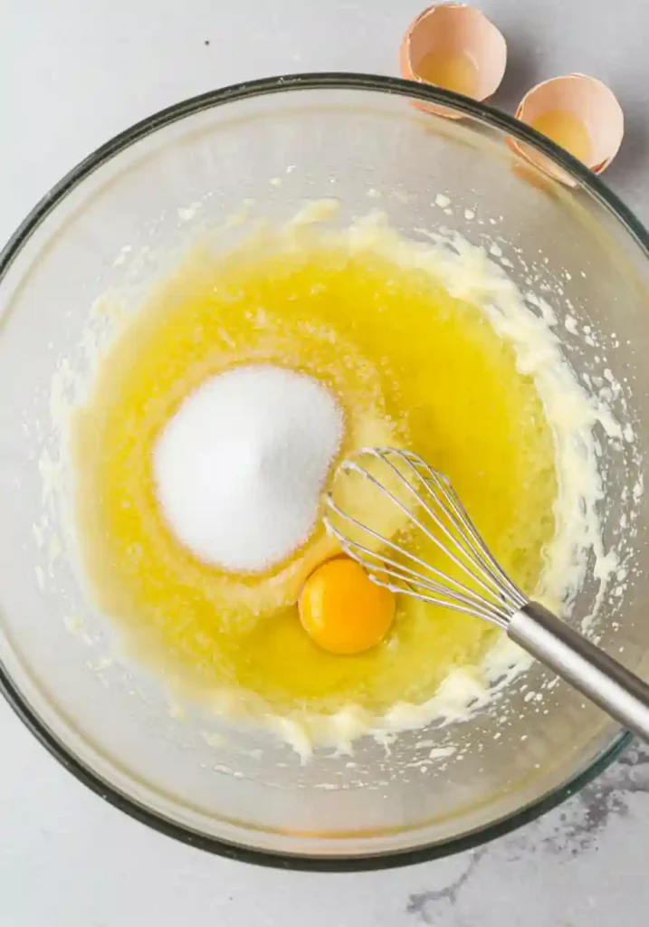 Large mixing bowl with melted butter, sugar, eggs and milk being whisked together for apple fritter bread batter