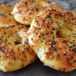Four golden-brown cottage cheese bagels in air fryer basket, topped with everything seasoning, showing perfect texture and color