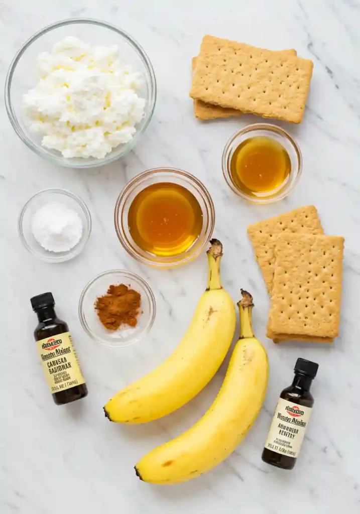 Cottage cheese, bananas, honey, vanilla, cinnamon and graham crackers arranged on white marble surface