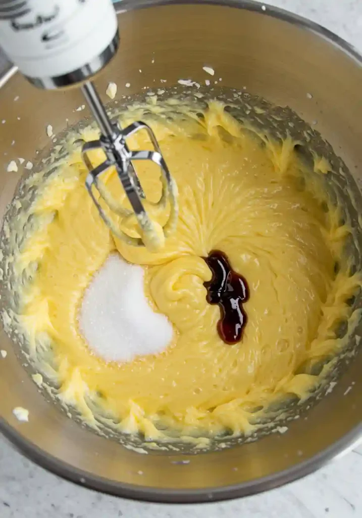 Electric mixer whisking eggs and sugar until light and fluffy for madeleine cookies recipe, showing pale yellow doubled volume mixture