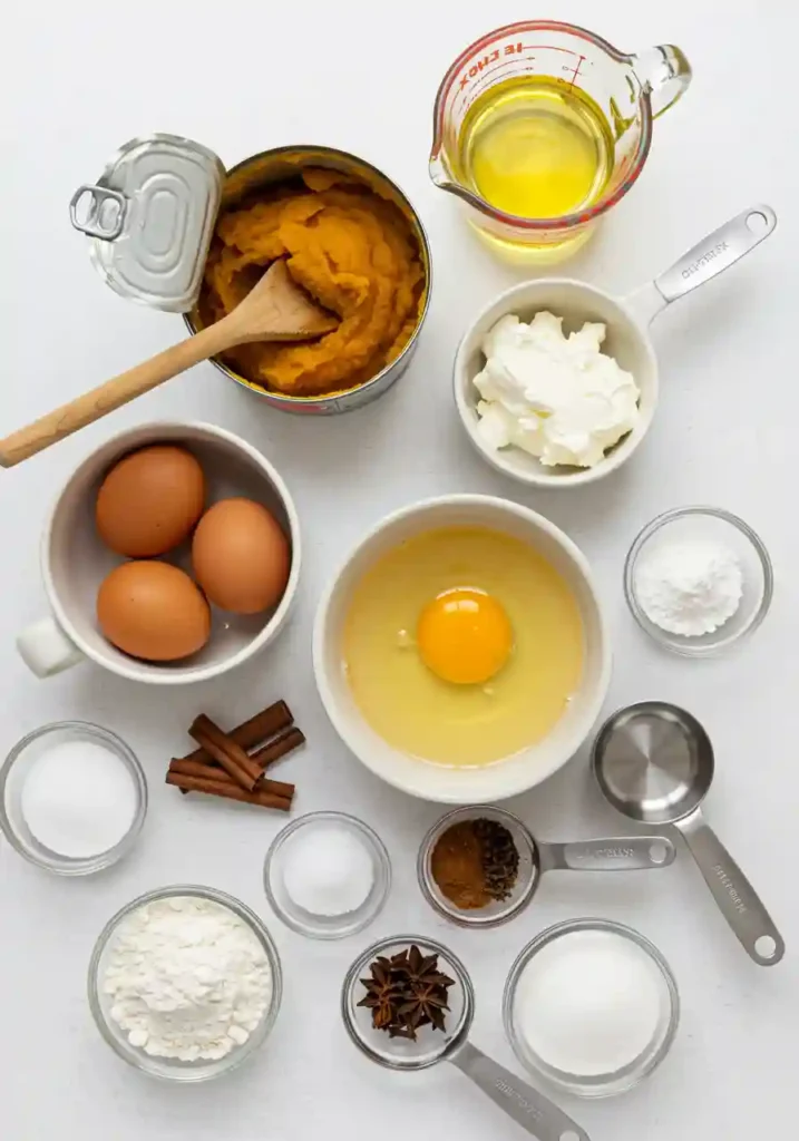 All ingredients for pumpkin bread with cream cheese recipe laid out on white counter including pumpkin puree and spices