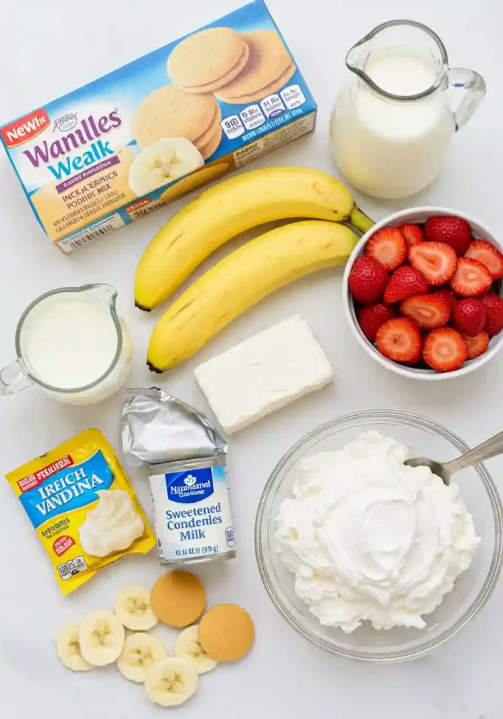 All ingredients for strawberry banana pudding arranged on counter including vanilla wafers, fresh strawberries, bananas, cream cheese, pudding mix, milk and whipped topping