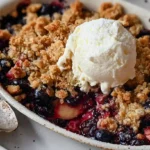 Apple blueberry crisp with golden brown oat topping in white baking dish served with vanilla ice cream