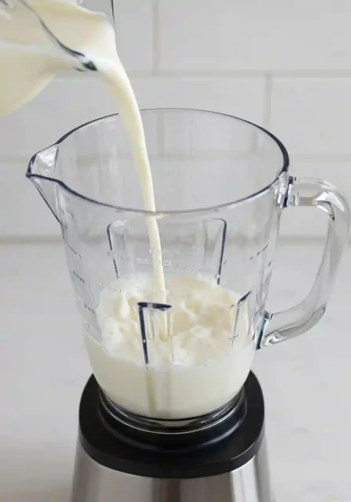 Milk being poured into blender pitcher as first step for making chocolate banana smoothie