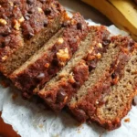 Sliced gluten free banana bread on wooden board showing moist texture with walnuts