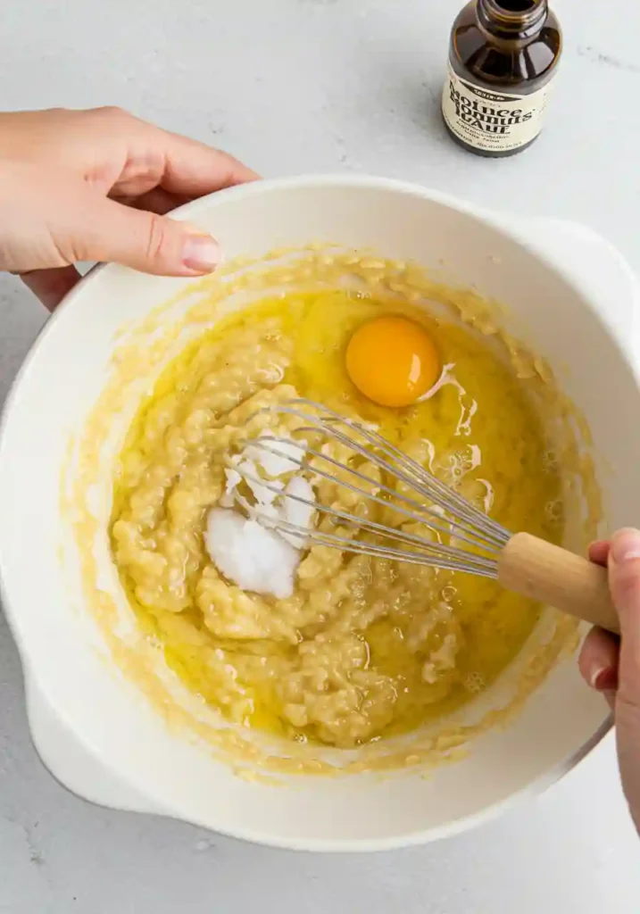 Whisking mashed bananas with eggs and coconut oil in white bowl for gluten free banana bread batter