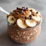 Chocolate peanut butter overnight oats in a mason jar topped with chocolate chips and peanut butter drizzle on a marble counter