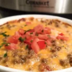 Creamy rotel dip with ground beef in white slow cooker surrounded by tortilla chips on wooden board