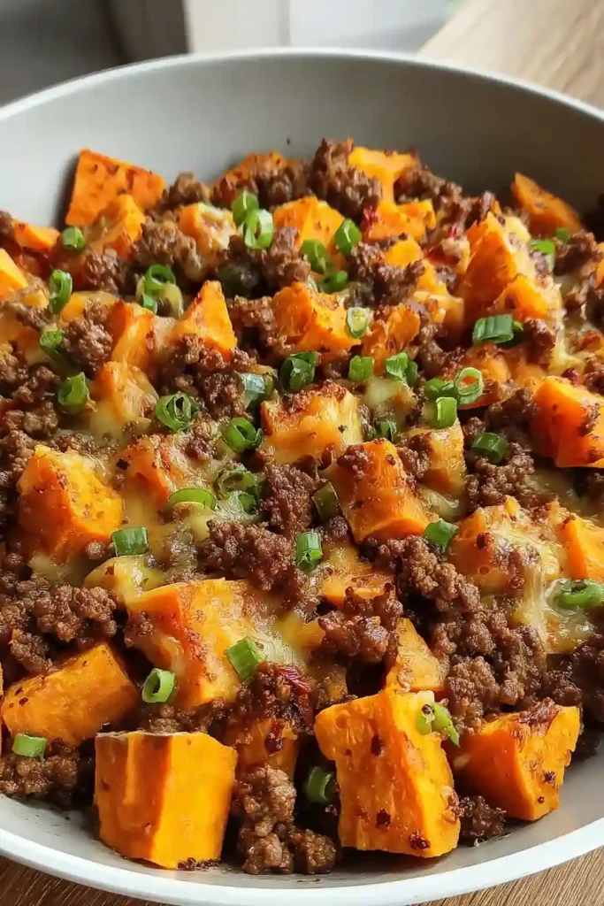Shredded cheese melting over cooked sweet potato and ground beef mixture in skillet