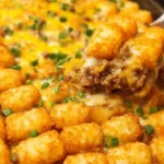 Tater tot casserole with ground beef topped with crispy golden tater tots, melted cheddar cheese, and fresh scallions in white baking dish