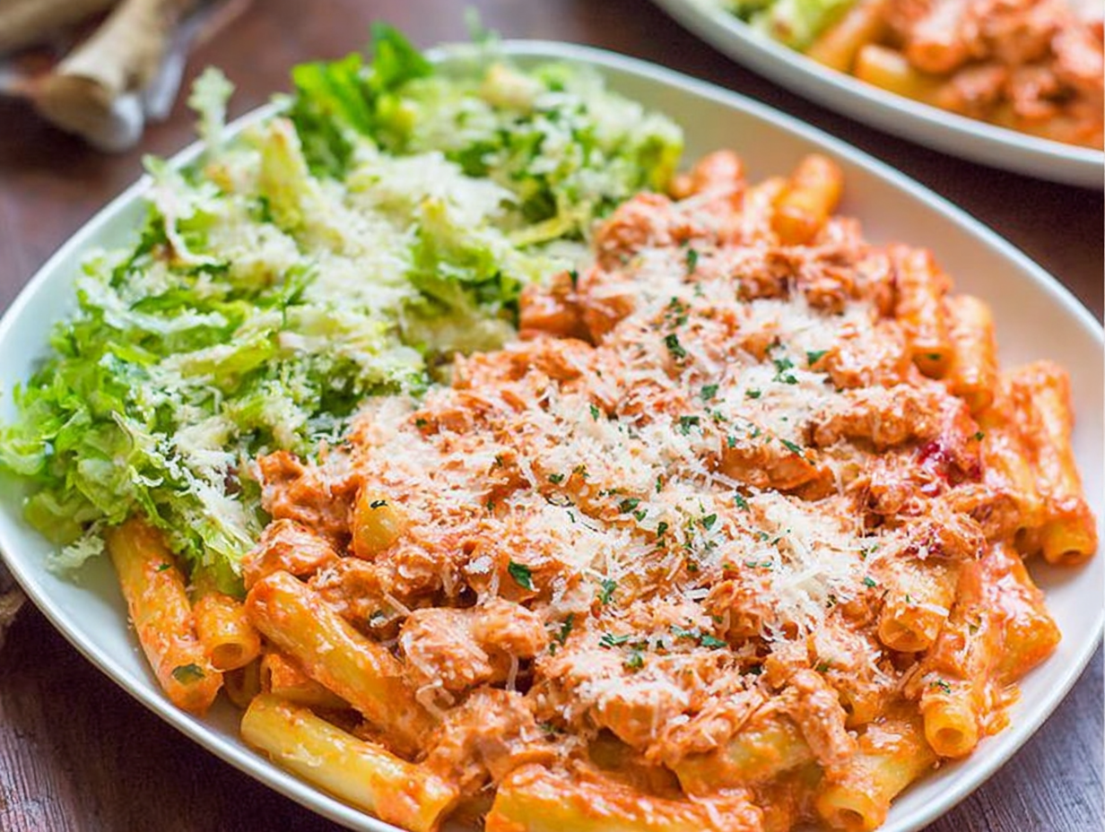 A close-up shot of a serving of five cheese ziti al forno in a white bowl, showing the melted cheese and crispy breadcrumb topping.